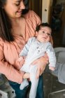 Молода мати тримає на руках новонароджену дитину, стоячи вдома — стокове фото
