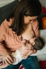 D'en haut jeune mère tenant sur les mains et l'allaitement nouveau-né enveloppé dans une couverture sur le lit à la maison — Photo de stock