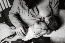 De cima jovem mãe segurando as mãos e amamentando bebê recém-nascido envolto em cobertor na cama em casa — Fotografia de Stock