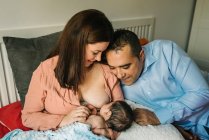Dall'alto madre e padre senza volto che si tengono per mano e allattano il neonato avvolto in una coperta sul letto a casa — Foto stock