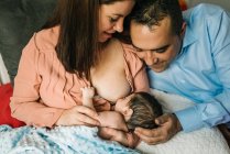 From above faceless mother and father holding on hands and breastfeeding newborn baby wrapped in blanket on bed at home — Stock Photo