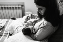 From above young mother holding on hands and breastfeeding newborn baby wrapped in blanket on bed at home — Stock Photo