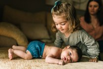 Cute little girl caring innocent newborn baby in back lying on sofa at home — Stock Photo