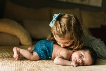 Linda niña besando bebé recién nacido inocente en la espalda tumbado en el sofá en casa - foto de stock