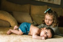 Cute little girl caring innocent newborn baby in back lying on sofa at home — Stock Photo