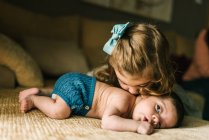 Cute little girl kissing innocent newborn baby in back lying on sofa at home — Stock Photo