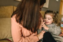Faceless giovane madre abbracciando allegra figlioletta considerando mano seduta sul divano a casa — Foto stock