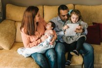 Glückliche junge Mutter hält Neugeborenes in Decke gewickelt und Vater hält Tochter zu Hause auf Sofa — Stockfoto