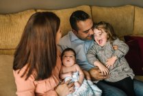 Glückliche junge Mutter hält Neugeborenes in Decke gewickelt und Vater hält Tochter zu Hause auf Sofa — Stockfoto
