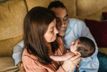 Glückliche junge Mutter hält Neugeborenes in Decke gewickelt und Vater sitzt zu Hause neben ihnen auf Sofa — Stockfoto