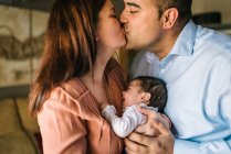 Glückliche Eltern küssen sich, während sie weinendes Baby zu Hause halten und umarmen — Stockfoto