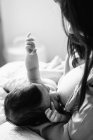 D'en haut jeune mère tenant sur les mains et l'allaitement nouveau-né enveloppé dans une couverture sur le lit à la maison — Photo de stock