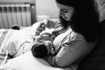 De cima jovem mãe segurando as mãos e amamentando bebê recém-nascido envolto em cobertor na cama em casa — Fotografia de Stock
