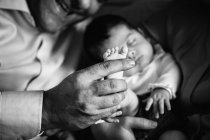 Sorrindo pai segurando rindo pequena filha deitada na cama com a mãe segurando bebê recém-nascido — Fotografia de Stock