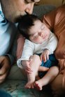 Улыбающийся отец держит смеющуюся маленькую дочь лежащую на кровати с матерью, держащей новорожденного ребенка — стоковое фото