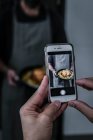 Обрізати людину рука фотографує на мобільному телефоні смачна страва в руках безликого чоловіка — стокове фото
