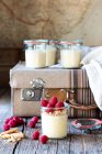 Composition of old suitcase and glass tubs with cheesecake and raspberries placed on wooden table — Stock Photo