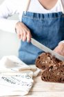 Hands of woman in apron cutting rye bread with raisins and nuts — Stock Photo