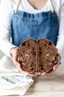 Hands of woman in apron holding rye bread with raisins and nuts — Stock Photo