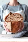 Mãos de mulher em avental de cozinha com ambas as mãos cortando pão caseiro — Fotografia de Stock