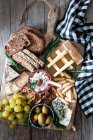 Сверху композиция свежего ржаного хлеба, сыра, винограда и оливок помещена на деревянную доску — стоковое фото