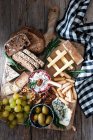 Dall'alto composizione di pane di segale fresco, formaggio, grappolo d'uva e olive messe su asse di legno — Foto stock