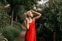 Seitenansicht der attraktiven Blondine in rot sinnlich posiert mit geschlossenen Augen zwischen grün blühenden Bäumen — Stockfoto