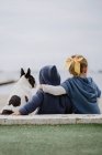 Погляд на двох дітей, які обіймають французького бульдога, сидячи на березі моря. — стокове фото