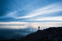 Silhouette of woman standing on rocky coastline at sunset in Wales — Stock Photo