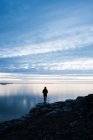 Silhueta de mulher em pé na costa rochosa ao pôr do sol no País de Gales — Fotografia de Stock