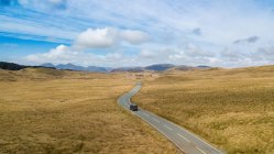 Автомобиль едет по одинокой асфальтовой дороге в горной местности в солнечный день в Уэльсе — стоковое фото