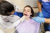 Dentista femenina que atiende a la paciente con su asistente - foto de stock