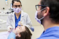 Dentista feminina que atende paciente com seu assistente — Fotografia de Stock