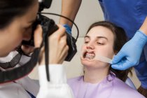 Женщина-дантист с ассистентом ухаживает за пациентом, фотографирует зубы пациента — стоковое фото