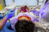 Dentista y su asistente usando la lámpara ultravioleta en la dentadura postiza del paciente - foto de stock
