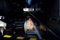 Приваблива жінка-солдат дивиться на камеру, сидячи всередині темного ангара — стокове фото