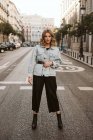 Стильна жінка в модному вбранні, що стоїть посеред асфальтової дороги на міській вулиці — стокове фото