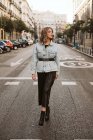 Приваблива жінка в модному вбранні, що стоїть посеред асфальтової дороги на міській вулиці — стокове фото