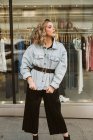 Attraktive junge Frau in stylischem Outfit schaut weg mit Klamotten Schaufenster hinter auf der Straße der Stadt — Stockfoto