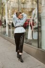 Приваблива молода жінка в стильному вбранні дивиться на одяг за вікном магазину під час прогулянки по міській вулиці — стокове фото