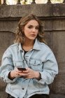 Ritratto di giovane signora in elegante vestito smartphone di navigazione mentre seduto vicino alla recinzione di pietra del parco della città — Foto stock