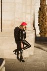 Stylische junge Frau trägt trendige rote Baskenmütze und blickt in die Kamera, während sie an einem sonnigen Tag auf der Straße steht — Stockfoto