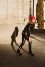 Стильна молода жінка в модному червоному береті і дивиться на камеру, стоячи на вулиці міста в сонячний день — стокове фото