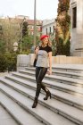 Junge Frau mit stylischer roter Baskenmütze schaut weg, während sie auf der Stadtstraße die Treppe hinuntergeht — Stockfoto