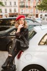 Giovane donna in abito alla moda che calpesta la valigia mentre si appoggia sulla macchina — Foto stock
