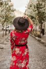 Visão traseira da jovem mulher em vestido elegante e chapéu andando no pavimento envelhecido na rua da cidade — Fotografia de Stock