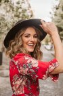 Сміється молода жінка в стильне плаття і капелюх дивлячись на камеру у віці тротуар на міській вулиці — стокове фото