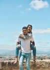 Verliebtes Paar genießt einen sonnigen Sommertag, während es lacht und Schultern trägt — Stockfoto