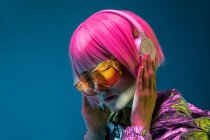 Junge Asiatin mit stylischem rosa Haarschnitt und funkelnder silberner Jacke steht und genießt Musik — Stockfoto