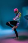 Jovem mulher asiática com corte de cabelo rosa elegante e jaqueta de prata brilhante de pé em uma perna e ouvir música — Fotografia de Stock